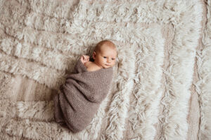 Nyfødt baby med våkent blikk. Pakket inn i et teppe